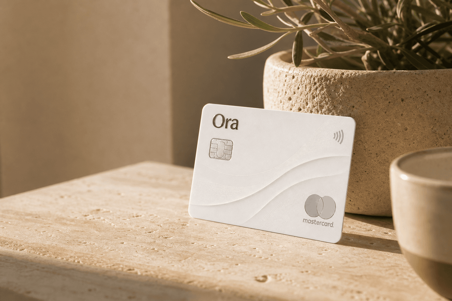 An Ora card resting on a sunlit travertine surface beside an olive plant